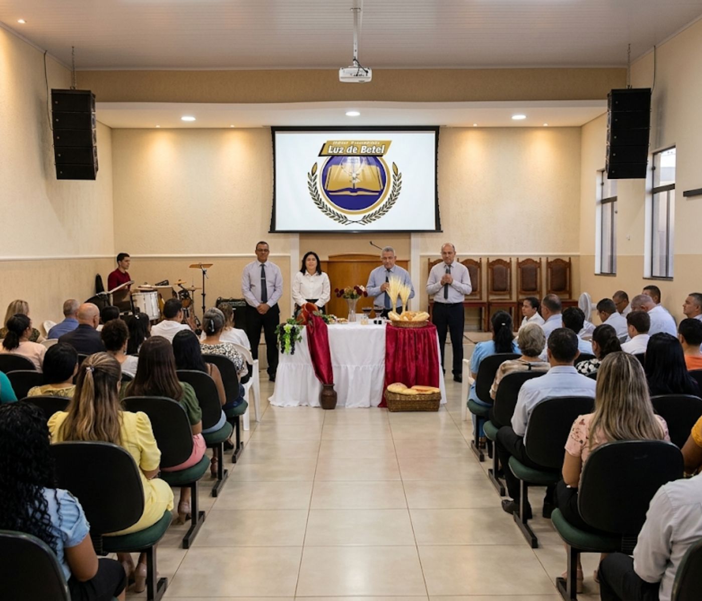Visão interna do templo da Igreja Luz de Betel em Ourinhos durante celebração, com fiéis sentados, mesa de Santa Ceia ornamentada e liderança ao fundo sob iluminação quente e profissional.